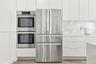 Kitchen featuring high-gloss white cabinetry, stainless steel double wall ovens, a stainless steel French-door refrigerator, stone-composite backsplas