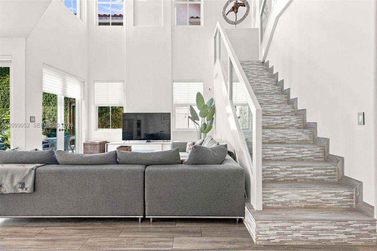 Double-height ceiling, open floor plan featuring wood-finish flooring, staircase with tiled risers, white railing, and glass paneled walls, and multip