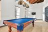 Vaulted ceiling with exposed wood beams, triple-pendant brass lighting fixture, and multiple tall windows