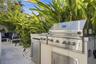 Outdoor kitchen featuring a stainless steel grill, stone-surfaced countertops, custom built-in cabinetry, and integrated storage, set against a landsc