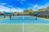 Hard-court tennis facility featuring blue and green surface, permanent net, protective perimeter fencing, pole-mounted lighting, and integrated shaded