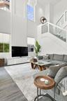 High-ceiling interior featuring multiple oversized windows, wood-finish flooring, glass-panel stair railing, and a tiered spherical chandelier