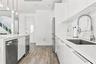 Kitchen featuring high-gloss white cabinetry, white stone countertops, integrated stainless steel appliances, a pull-down commercial-style faucet, and