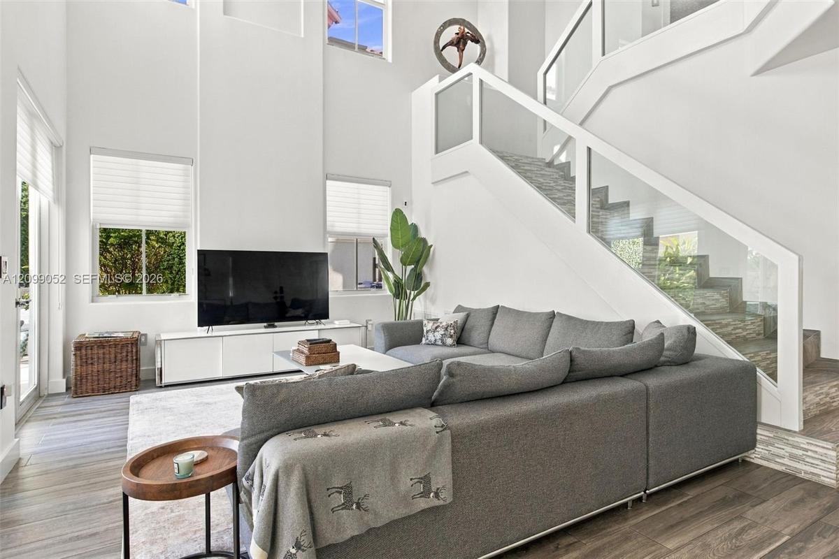 Double-height ceiling, glass-paneled staircase railing, wood-finish flooring, and expansive windows