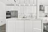 Kitchen featuring high-gloss white cabinetry, a waterfall-edge stone island, stainless steel built-in double wall ovens, a coordinating range hood, an