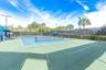 Tennis court featuring a multi-tone hard surface, perimeter fencing, overhead lighting, and shaded seating areas