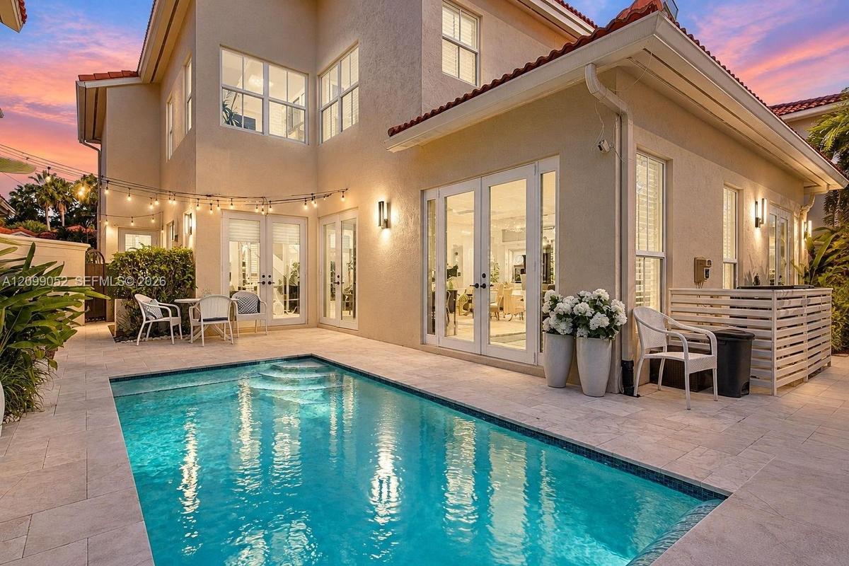 Stucco exterior featuring multiple sets of glass-paneled double doors, stone-tiled patio, and a built-in swimming pool