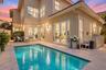 Stucco exterior featuring multiple sets of glass-paneled double doors, stone-tiled patio, and a built-in swimming pool