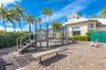 Recreational area featuring a multi-component play structure, wood-chip surface, built-in bench seating, and landscaped perimeter hedges