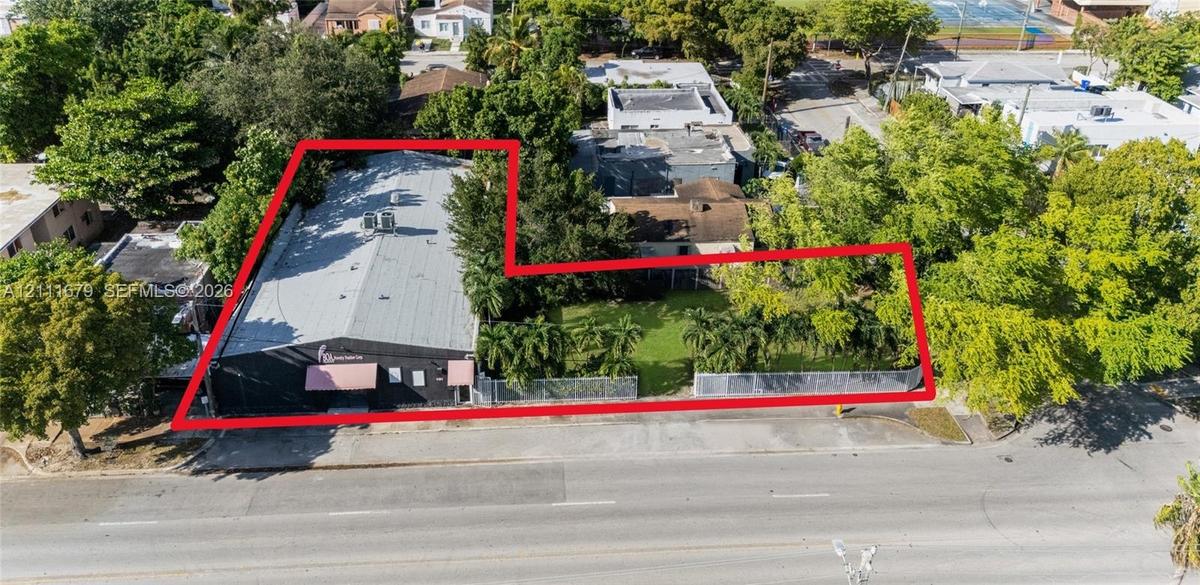 Expansive parcel featuring a structured building, generous green space, mature trees, palm trees, and perimeter fencing