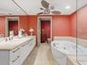 Dual-sink vanity with stone countertop, recessed lighting, jetted soaking tub, glass-enclosed shower, and stone-finish flooring