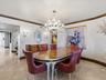 Ornate multi-tier crystal chandelier, built-in wooden sideboard with stone countertop, crown molding, stone tile flooring, and wall-mounted sconces