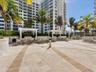 Stone-paved terrace featuring multiple white pergolas, built-in outdoor cooking stations, and mature palm landscaping