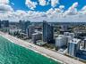 Aerial perspective of a coastal high-rise district featuring direct sandy shoreline access, multiple oceanfront structures, and extensive metropolitan
