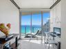 Floor-to-ceiling sliding glass doors, private balcony, neutral stone-finish flooring, and multi-pendant lighting fixture