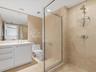 Bathroom featuring a walk-in shower with stone-tile surround, polished chrome fixtures, white vanity with integrated countertop and sink, and a large 
