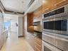 Kitchen featuring flat-panel wood cabinetry, integrated stainless steel double wall ovens, a glass cooktop, dark stone countertops, and stone tile flo