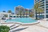 Resort-style pool featuring a curvilinear design, stone tile decking, integrated structural shade pavilion, and surrounding palm landscaping