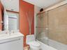 Bathroom featuring a white vanity cabinet with an integrated sink, polished metal widespread faucet, and a shower-tub combination enclosed by glass sl