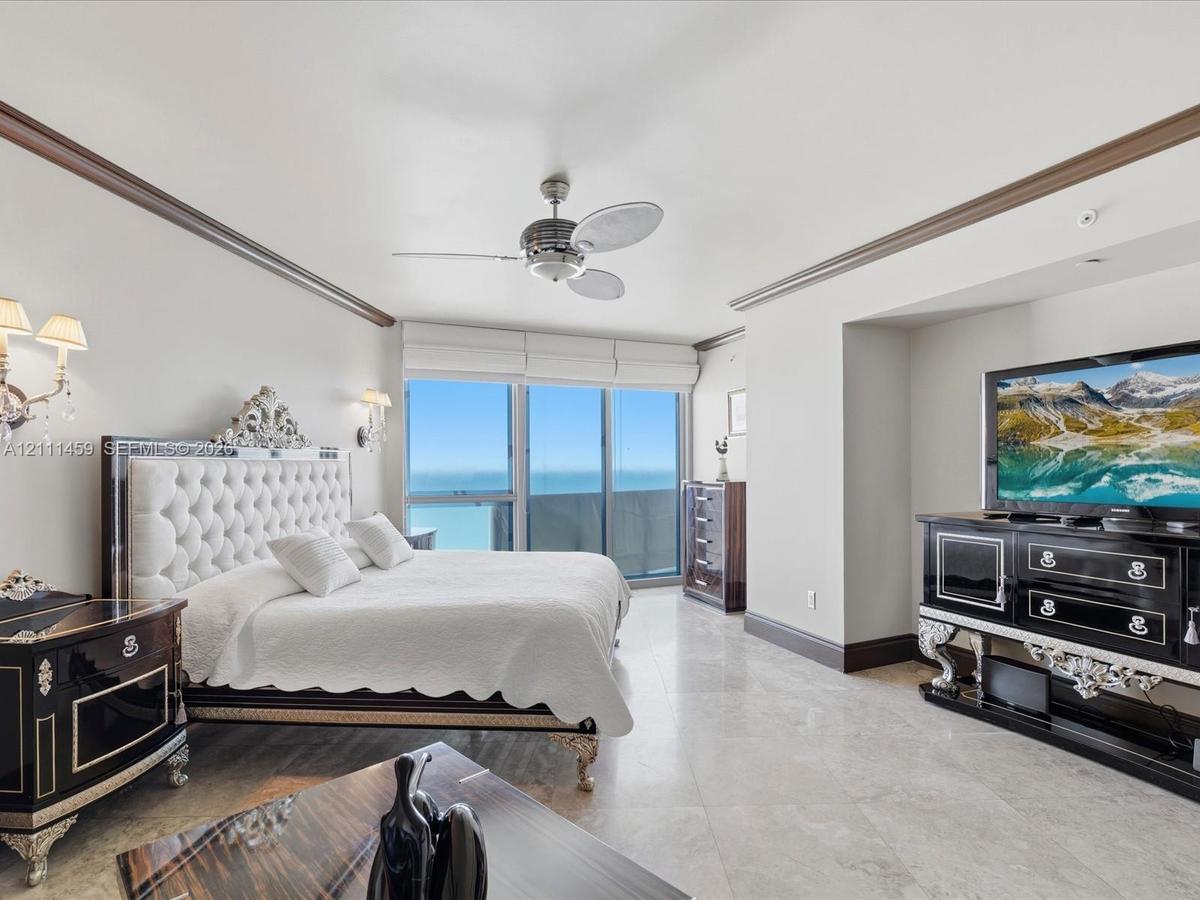Floor-to-ceiling windows, polished stone flooring, crown molding, wall-mounted light fixtures, and a ceiling fan