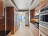 Galley kitchen featuring custom flat-panel wood cabinetry, black stone countertops, integrated stainless steel refrigeration, built-in double ovens, a