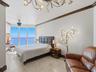 Floor-to-ceiling windows featuring ocean horizon, neutral stone flooring, decorative crown molding, and intricate multi-light chandelier