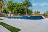 Custom pool featuring a raised tiled spillway, light-toned stone paver decking, integrated grass inlay accents, and a metal perimeter fence