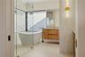 Freestanding soaking tub, frameless glass-enclosed shower, wall-mounted wood-finish vanity, stone countertop, and brass-tone plumbing fixtures