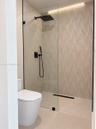 Walk-in shower featuring a frameless glass enclosure, patterned tile accent wall, matte black rainfall showerhead, integrated handheld sprayer, and li