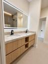 Double vanity featuring light wood-finish cabinetry with open shelving, stone countertop, matte black fixtures, and a large LED-backlit mirror