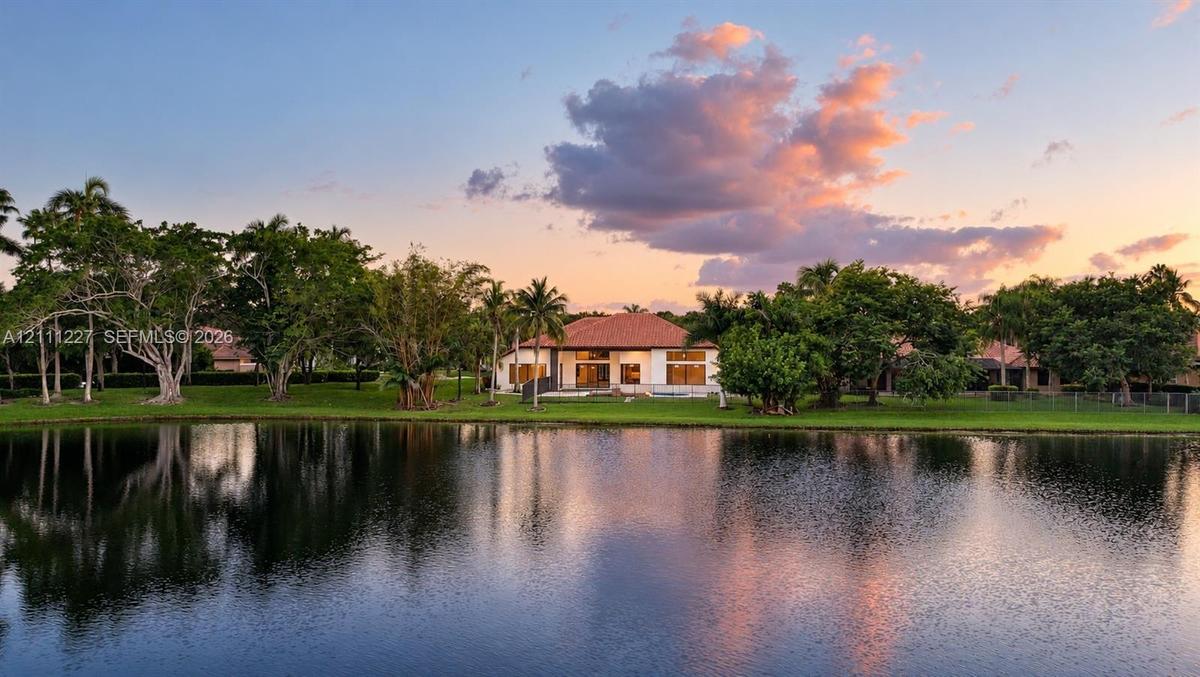 Waterfront residence featuring a tile roof, expansive lawn, mature landscaping, and palm trees