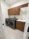 Utility room featuring wood-finish cabinetry, a built-in sink with a stone-surfaced countertop, and neutral tile flooring