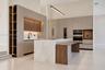 Modern kitchen featuring flat-panel cabinetry, a waterfall-edge stone island with an integrated wood-finish breakfast bar, built-in double ovens, and 