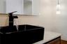 Matte black waterfall faucet, rectangular vessel sink, stone countertop, wood-finish cabinetry, and contemporary pendant lighting