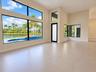 High-ceilinged living space featuring expansive floor-to-ceiling windows, large-format tile flooring, black-framed glass entry door, and water-facing 