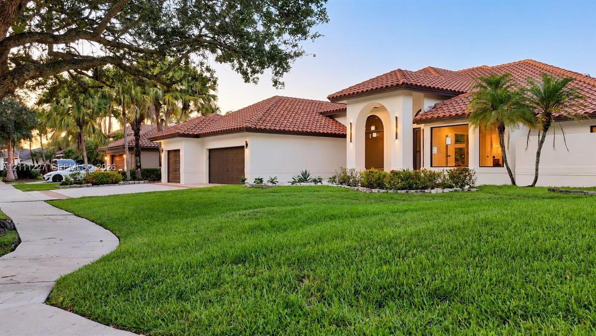 Stucco exterior featuring a terracotta tile roof, arched entryway, multi-car garage, and manicured landscaping