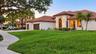 Stucco exterior featuring a terracotta tile roof, arched entryway, multi-car garage, and manicured landscaping