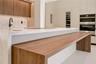 Kitchen featuring a waterfall-edge island with wood-finish counter seating, integrated stainless steel appliances, full-height cabinetry, stone-finish