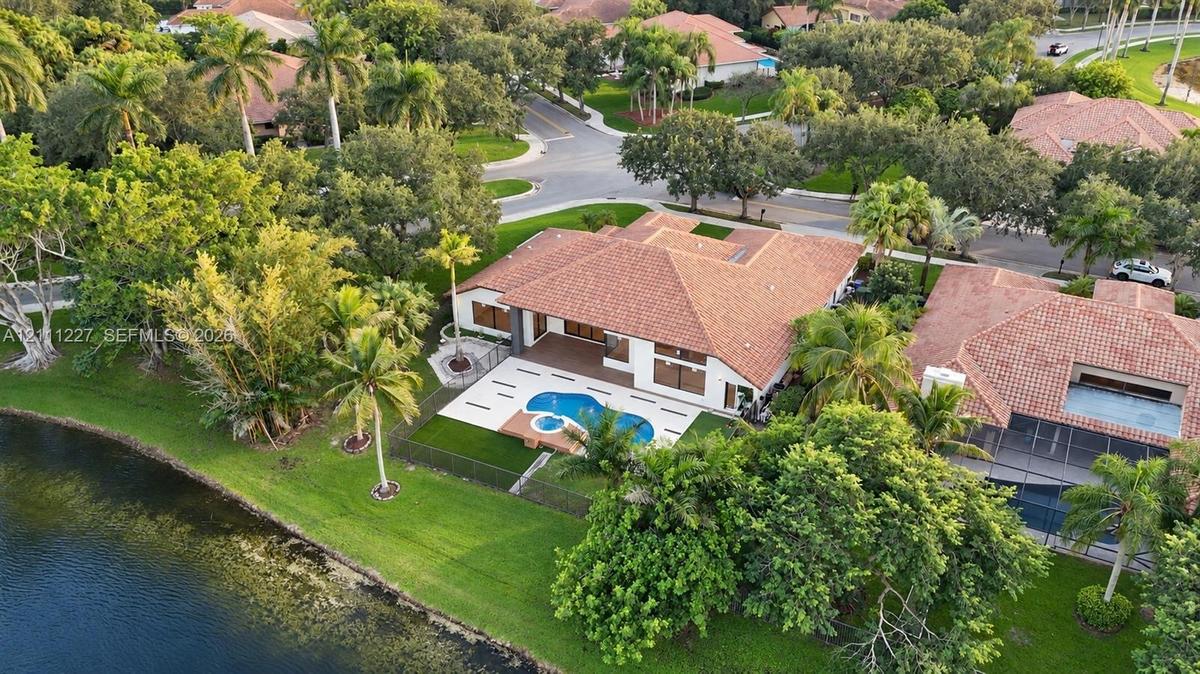 Aerial perspective of a single-story residence featuring a tile roof, a rear patio with an inset swimming pool and spa, and expansive lawn space with 