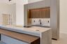Modern kitchen featuring full-height flat-panel cabinetry, a wood-finish recessed upper cabinet section with integrated under-cabinet lighting, a wate