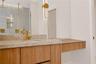 Floating vanity with wood-finish cabinetry, stone countertop, integrated sink, brass-toned fixtures, and vertical wall-mounted lighting
