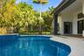 Custom swimming pool with blue tile finish, stone paver decking, covered patio, metal perimeter fencing, and mature landscaping