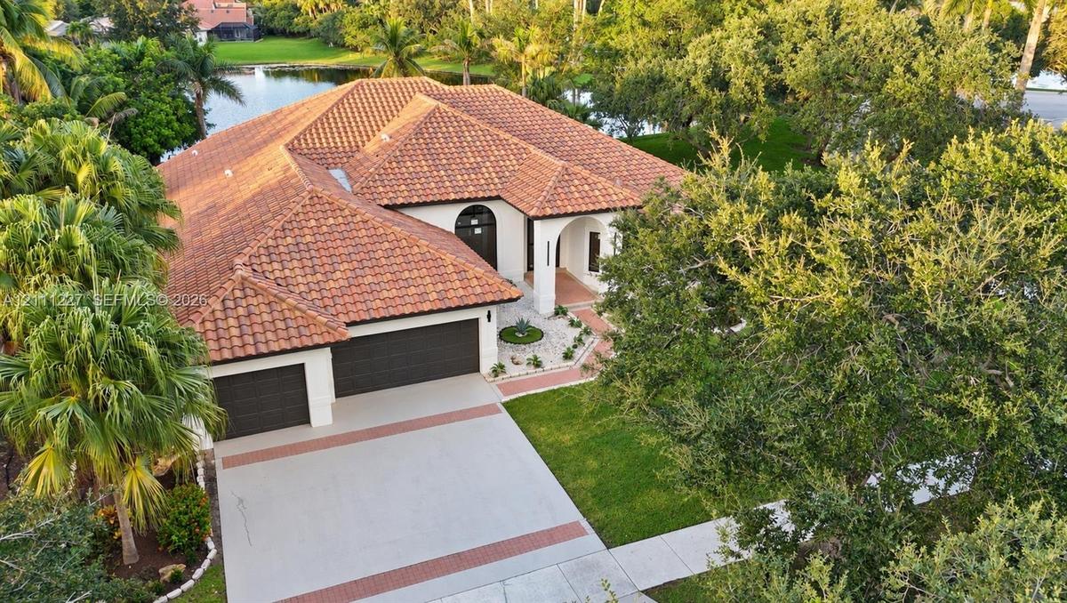 Mediterranean-style residence featuring a multi-pitched clay tile roof, stucco exterior, two-car garage, concrete driveway with decorative brick inlay