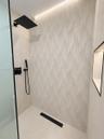 Walk-in shower featuring patterned large-format wall tile, matte black rainfall and handheld showerheads, integrated recessed niche lighting, and a li
