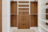Custom walk-in closet featuring wood-finish cabinetry, built-in shelving, integrated hanging rods, and a four-drawer dresser unit with matte hardware