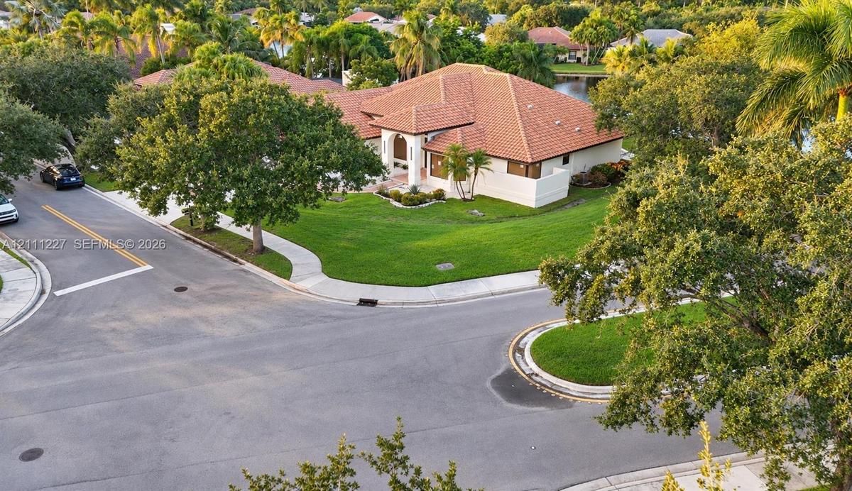 Corner lot property featuring a multi-gabled terracotta tile roof, stucco exterior, expansive lawn, and mature landscaping