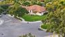Corner lot property featuring a multi-gabled terracotta tile roof, stucco exterior, expansive lawn, and mature landscaping