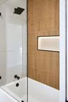 Walk-in shower enclosure featuring floor-to-ceiling vertically textured tile, a built-in recessed niche, a matte black rainfall shower head, and match