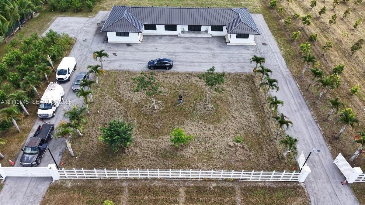 Single-story residence featuring a dark metal roof, expansive grounds, paved driveway, and perimeter fencing
