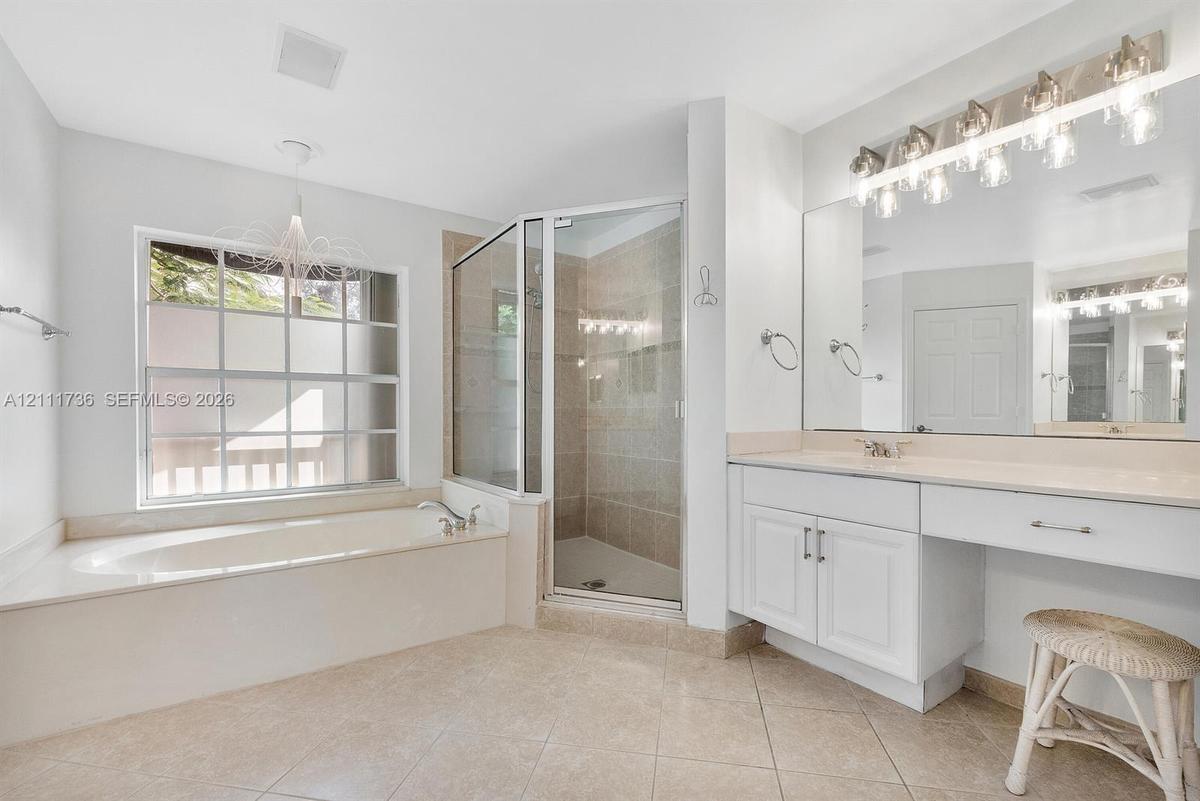 Bathroom featuring a built-in soaking tub, a tiled glass-enclosed shower, dual-basin vanity with solid-surface countertops, and large wall-mounted mir